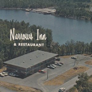 Aerial view of multi-story building surrounding parking lot with cars and main road leading to bridge over a lake