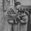 Older white woman in head wrap and shawl leaning down at young boy in coat to take cigarette from his mouth