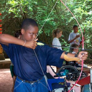 Young black boy drawing bow and arrow back with other children in background