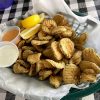 Basket of fried breaded pickle slices with two sauces and lemon slices on side