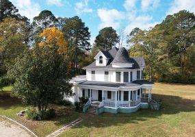Multistory house with steps leading to wrap around porch in large yard and tree in front near entrance