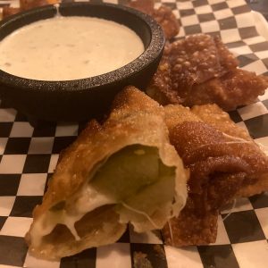 Breaded dill pickles with cheese inside next to small sauce cup with ranch on food tray
