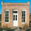 Single story brick building two windows on either side of wooden door