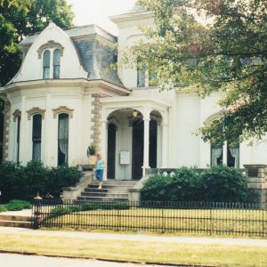 Elaborate multistory manor house with arched windows and iron fence