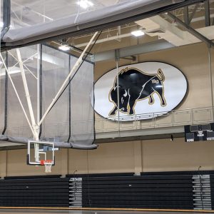 View of illustrated bison mascot sign above basketball court with goal scoreboard and bleachers