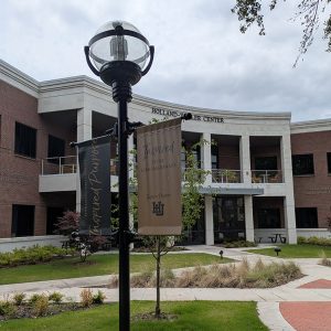 Light pole with banners next to concrete walkway in front of two story brick and stone building with second floor balcony and seating