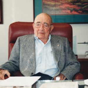older white man wearing glasses dress shirt and suit jacket sitting on leather chair at desk in office