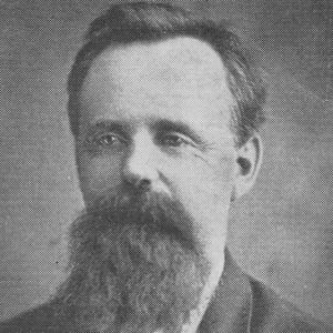 White man with short hair and long beard dressed in suit and white dress shirt