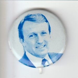 Round button with photo of white man from shoulders up dressed in suit clean shaven smiling