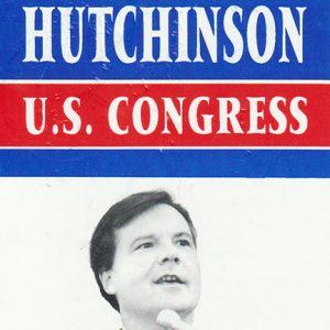 White man dressed in suit and tie speaking into microphone between texts "Hutchinson U.S. Congress" and "This is no time for silence"