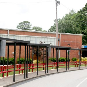View from road of single story brick building behind sidewalk lined with benches and metal covered walkway canopies