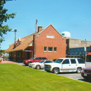Side view of single story brick building with three windows on facing parking lot next to large grass yard