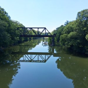 Metal railroad bridge standing over river large group of trees on either side